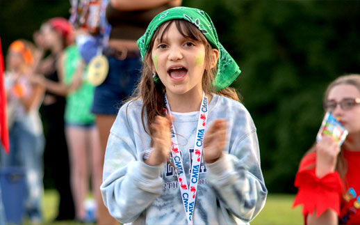 A child clapping at a CMTA outdoor event with other children in the background